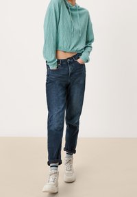 Hoodie corto turchese con una finitura testa, abbinato a jeans dritti blu scuro e sneakers alte bianche.