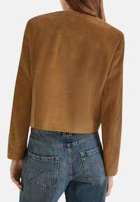 Giacca in velluto a coste marrone con strisce verticali, caratterizzata da maniche lunghe e orlo dritto, abbinata a jeans in denim blu.