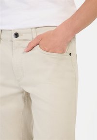 Beige Hosen mit klassischem Fünf-Taschen-Design, gefertigt aus leichtem Baumwollstoff mit leicht texturiertem Finish und dunkler Knopfverzierung.