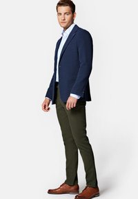 Granatowy, teksturowany żakiet na jasnoniebieskiej koszuli, w połączeniu z ciemnozielonymi, dopasowanymi spodniami i brązowymi skórzanymi butami.