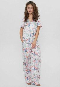Completo da loungewear con motivo floreale, composto da una maglietta a maniche corte e pantaloni a gamba larga in tessuto leggero. I colori dominanti includono rosa, blu e verde.