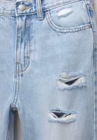 Jeans de mezclilla en un azul claro desgastado, con parches deshilachados, cierre de botón y diseño de cinco bolsillos. Los detalles de desgaste visibles realzan la textura.