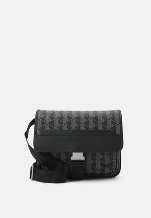 Zwarte Lacoste crossbodytas met geometrisch patroon, klepafsluiting, zilveren gesp en verstelbare schouderriem.