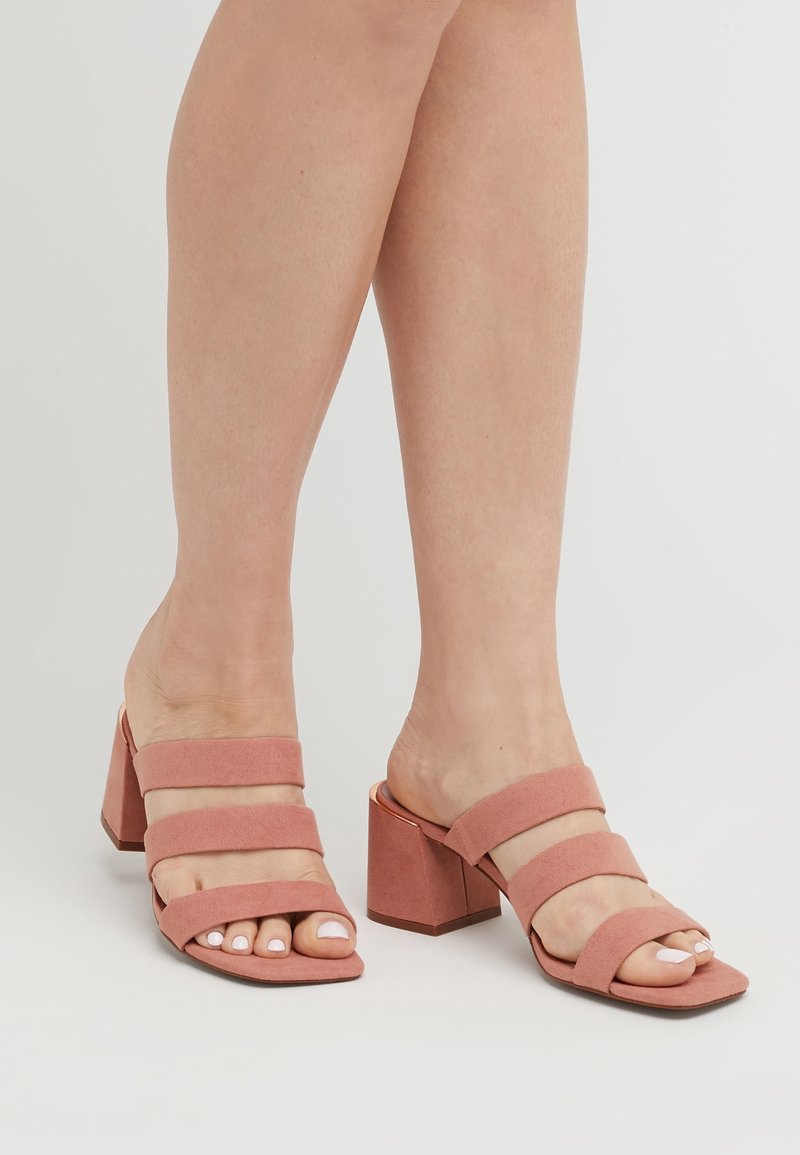 Mules en daim rose à talon bloc, avec trois larges brides. Design à bout carré, texture lisse et un talon robuste assurent stabilité et confort.