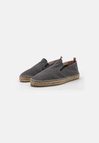 Espadrilles en toile grise avec une semelle en jute, design à enfiler, et accents contrastants rouges et bleus au niveau du talon. Texture lisse et forme arrondie.