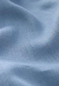 Tissu en lin bleu clair avec une texture douce, présentant un motif de tissage subtil et un tombé léger, créant une apparence fluide et lisse.