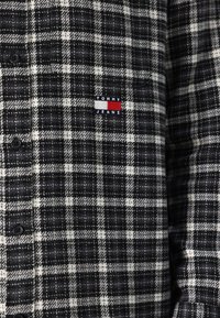 Juodai baltas languotas flanelinis marškinis su mažu "Tommy Jeans" logotipu, kuriame raudonos ir baltos juostelės ant krūtinės, šeši juodi mygtukai.