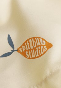 Satin-Stoff in hellem Creme zeigt ein Logo in Form einer orangefarbenen Zitrone mit blauen Blättern, dazu den Schriftzug "spitzbub studios" in Weiß.