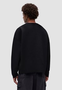 Svart oversized sweatshirt med rundad halsringning, sänkta axelsömmar och textilstruktur; bärs tillsammans med mörka cargobyxor.