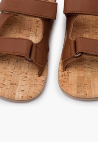 Brązowe skórzane sandały z dwiema regulowanymi paskami, korkową wkładką oraz teksturowaną powierzchnią. Posiadają metalowe elementy do regulacji pasków.