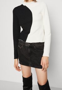 Langarmoberteil mit strukturiertem Design, gespaltenen Schwarz-Weiß-Farben, kombiniert mit einem schwarzen Denim-Rock und knielangen schwarzen Stiefeln.