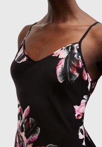 Svart blommig cami med tunna band, prydd med stora rosa och vita blommönster på tyget, slät textur och en figursydd design.