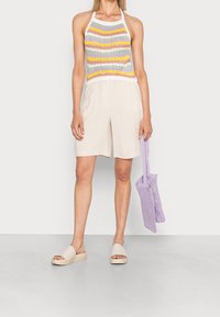 Top de crochet con tirantes y rayas multicolores; pantalones cortos de lino beige; bolso de malla ligero en color púrpura claro; sandalias sin hebillas color crema con una ligera plataforma.