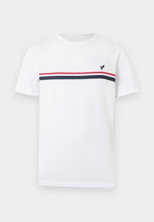 Bílé tričko s krátkým rukávem a kulatým výstřihem, s červenými a námořnicky modrými horizontálními pruhy a malým černým logem ptáka na levé straně hrudi.