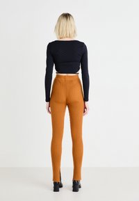 Zwarte lange mouwen cropped top met een gestructureerd patroon, gecombineerd met oranje geribbelde hoge taille broek met zijsplitten en een getailleerd silhouet.