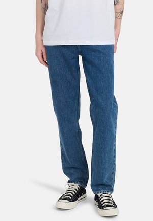 Blue denim jeans featuring a straight-leg cut, subtle fading, and five-pocket design, worn with black low-top sneakers.