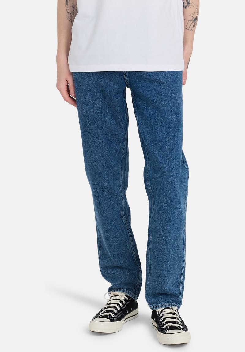 Jeans in denim blu con taglio dritto, leggermente sbiaditi, e design a cinque tasche, indossati con sneakers nere basse.