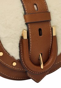 Bruine leren schouderband met gouden hardware accenten, voorzien van een donzig witte schapenvacht detail en zichtbare stiksels.