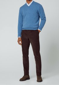 Pull bleu en laine à col en V, chemise blanche à col, pantalon en velours côtelé marron et bottes marron à lacets. Design simple avec poignets et ourlet côtelés.