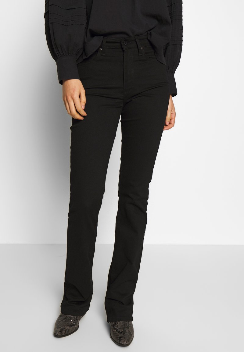 Flared black jeans with five-pocket design, belt loops, and a smooth fabric texture; worn with patterned ankle boots.