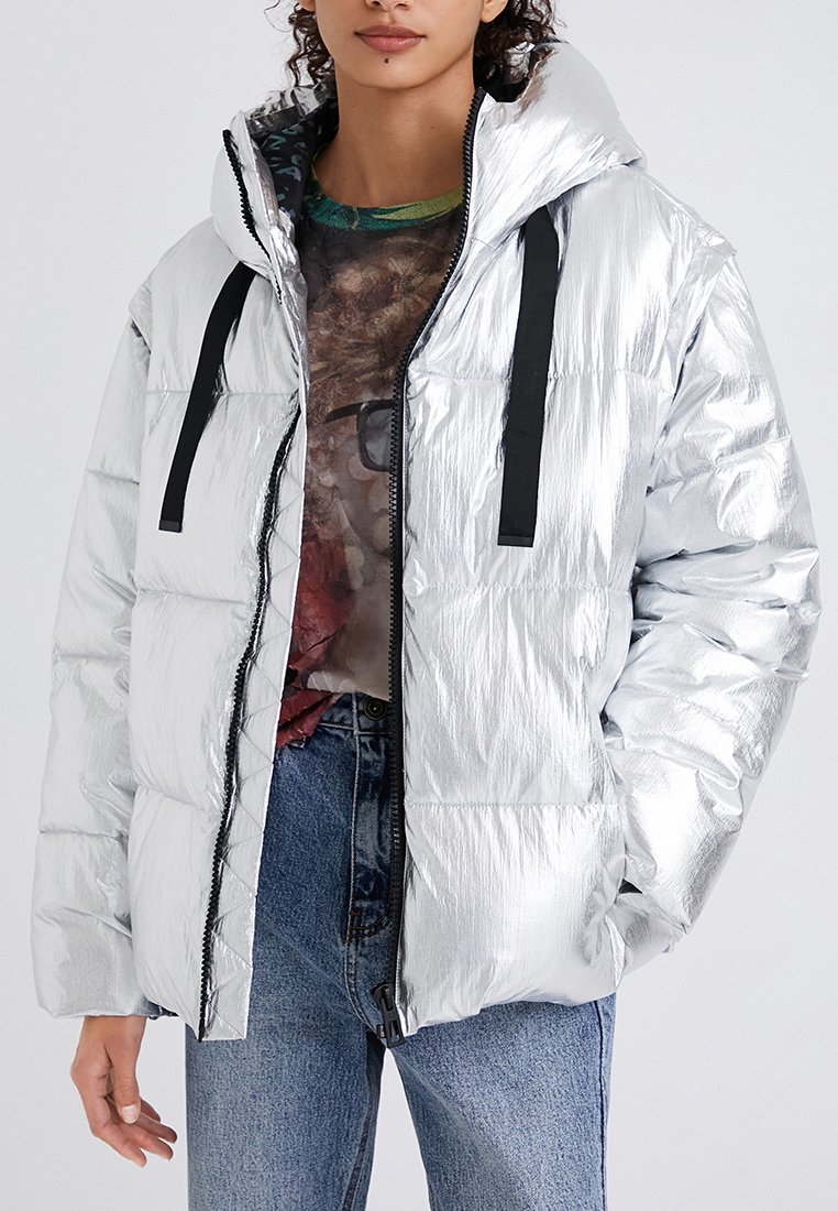 Srebrna metaliczna kurtka puchowa z kapturem, z czarnymi sznurkami, z przodu na zamek błyskawiczny i pikowanym wzorem. Noszona na wzorzystą koszulę.