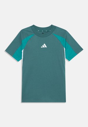 Tirkīza sporta t-krekls ar tumšākā tirkīza raglāna piedurknēm un baltu zīmola logotipu uz krūtīm. Mīksta auduma, ar apaļu kakla izgriezumu un īsām piedurknēm.