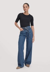 Zwart aansluitend T-shirt gecombineerd met hooggegeven blauwe denim palazzobroek met een ceintuur in de taille en steekzakken. Maat tot de vloer.