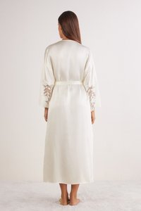 Lång cremefärgad satinrock med spetsdetaljer på de vida ärmarna, knytet i midjan, med en mjuk yta och ankellång design.