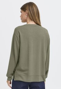 Sudadera de manga larga, color verde oliva, fabricada con un material suave. Presenta un cuello redondo y aberturas laterales en el dobladillo para mayor movilidad.