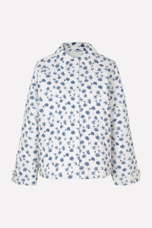 Veste matelassée avec un fond blanc et un motif floral bleu. Comprend un col, une fermeture à boutons, et des manches courtes avec des poignets retroussés.