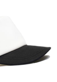 White and black baseball cap featuring a structured crown and a stiff, black brim with visible stitching detail. Textured fabric visible.