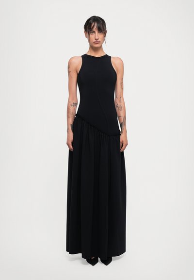 Abito nero con design senza maniche. Corpino aderente che si trasforma in una gonna fluida e arricciata. Tessuto liscio con decorazioni e cuciture minime.