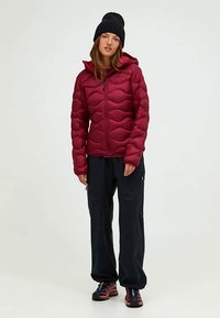 Burgundy puffer jacket with a wavy quilted design, zip closure, and hood, paired with dark pants and shoes featuring blue accents.