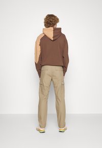 Ruskea ja beige väriblokkihuppari kengurun taskulla; yhdistetty vihreisiin cargo-housuihin, joissa on sivutaskut ja hillitty logo.