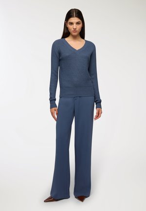 Maglione blu a collo a v lavorato a maglia con texture a coste abbinato a pantaloni blu a gamba larga. L'outfit presenta maniche lunghe e una silhouette rilassata.
