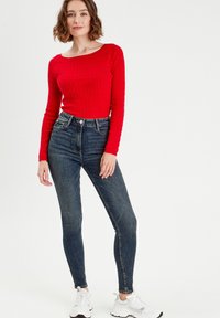 Czerwony sweter z długim rękawem o teksturowanym wzorze, w zestawie z ciemnoniebieskimi dżinsami typu skinny i białymi sportowymi butami. Prosty, codzienny design.