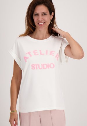Witte T-shirt met korte mouwen en roze, pluizige tekst "ATELIER STUDIO." Heeft een relaxte pasvorm en opgerolde mouwen. Glad katoenen stof.
