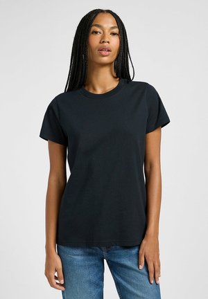 Camiseta de algodón negra con mangas cortas y escote redondo, exhibida sobre un fondo claro, combinada con jeans azules.