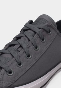 Σκούρο γκρι πάνινο αθλητικό παπούτσι με κορδόνια στο ίδιο χρώμα, μεταλλικά πόρπες και λευκό καουτσούκ σόλα με λεπτομέρεια μαύρης ρίγας.