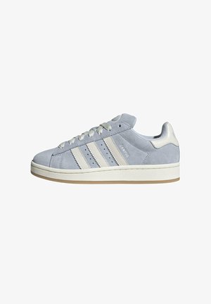 Světle šedá semišová teniska s bílou gumovou podrážkou, třemi bílými pruhy, tkaničkami a poutkem na patě, boční pohled.