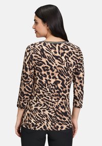 Haut en imprimé léopard avec des manches trois-quarts, présentant un tissu texturé beige et noir, agrémenté d'un détail de col contrasté.