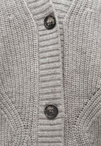 Hall halli kootud kardigan ribamustriga, millel on V-kaelus ja suur must nööp ees sulgemiseks.