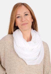 Écharpe blanche, légère et superposée, drapée autour du cou, avec une texture douce et transparente, complétant un pull en tricot beige.