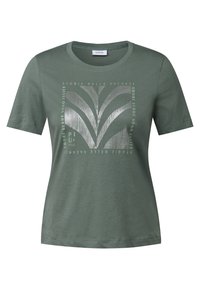 Grön kortärmad t-shirt med en stiliserad tryck med löv och text på flera språk, centrerad på framsidan.
