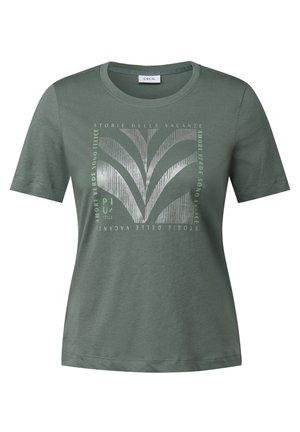 T-shirt à manches courtes verte avec un imprimé stylisé de feuilles et du texte en plusieurs langues, centré sur le devant.