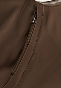 Pochette en nylon marron avec une fermeture éclair, présentant une texture lisse, des coutures soignées et une petite poche supplémentaire à l'intérieur.
