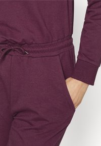 Completo jogger bordeaux con vita regolabile, polsini a coste e tasche laterali, realizzato in morbido tessuto di cotone con una texture liscia.