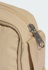 Borsa in tessuto beige dalla texture liscia, dotata di una cerniera argento con tirante. Il design include una cinghia laterale per una facile presa.