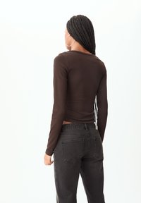 Haut marron à manches longues au design ajusté, associé à un jean noir taille haute avec poches arrière et une coupe légèrement ample.