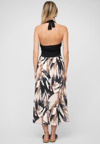 Haut noir à col halter avec une jupe fluide longueur cheville présentant un motif de feuilles abstrait en tan, noir et blanc ; tissu doux avec une coupe relaxed.
